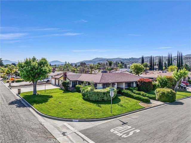 view of front of property featuring a garage, concrete driveway, a mountain view, a front yard, and a residential view