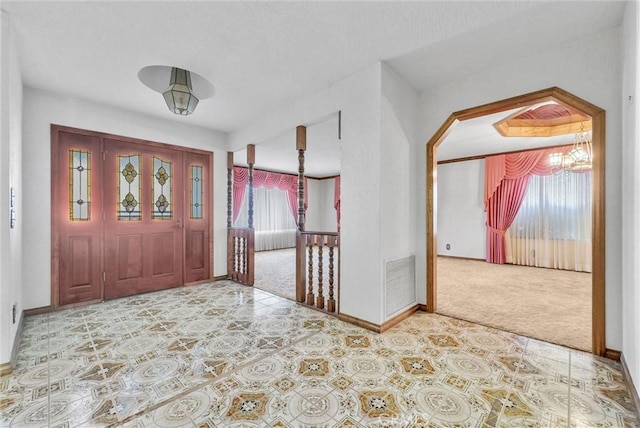 carpeted entrance foyer featuring plenty of natural light, baseboards, visible vents, and an inviting chandelier