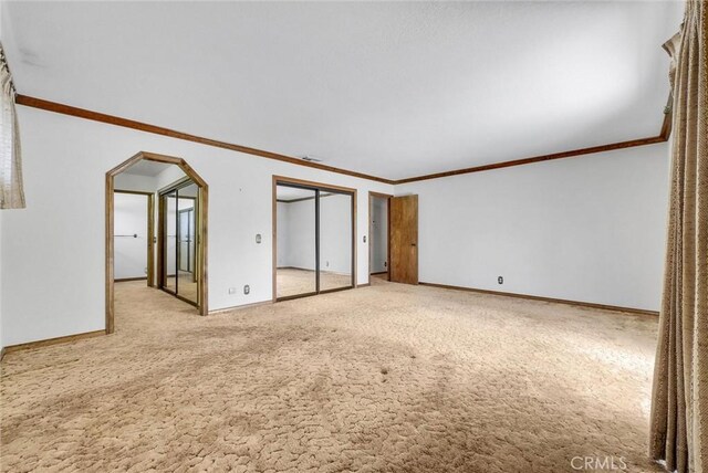 empty room featuring baseboards, arched walkways, light colored carpet, and crown molding
