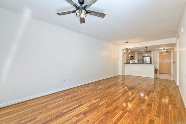 1150 J St Unit 117, San Diego, CA 92101 - unfurnished living room featuring light wood-type flooring, a chandelier, a ceiling fan, and baseboards