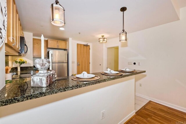 1150 J St Unit 117, San Diego, CA 92101 - kitchen featuring freestanding refrigerator, dark countertops, a peninsula, baseboards, and light wood finished floors