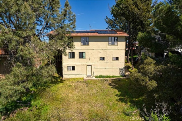 rear view of property with a lawn and roof mounted solar panels