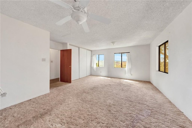 empty room with carpet floors, a ceiling fan, and a textured ceiling