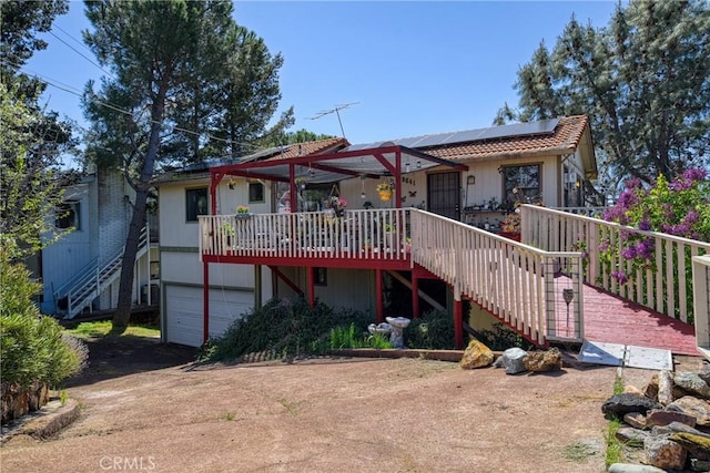 back of house with roof mounted solar panels, driveway, a garage, and stairway