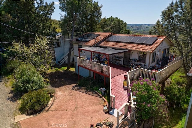 back of property with roof mounted solar panels, a wooden deck, concrete driveway, and a tiled roof