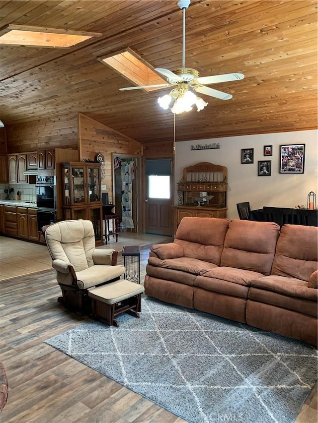 living area featuring light wood-style floors, ceiling fan, vaulted ceiling, wood ceiling, and wood walls