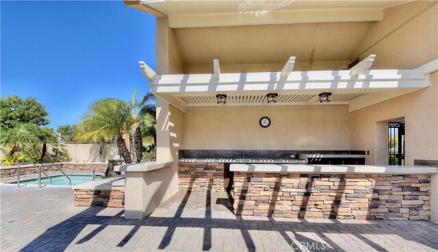 view of patio with fence, a swimming pool, outdoor wet bar, and exterior kitchen