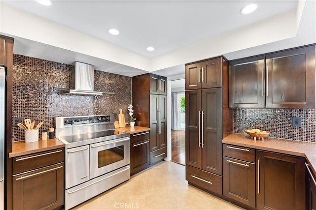kitchen with dark brown cabinets, wall chimney range hood, light countertops, backsplash, and double oven range