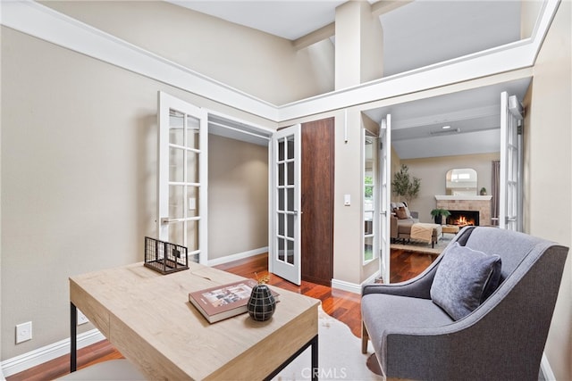 interior space with baseboards, french doors, a lit fireplace, and wood finished floors