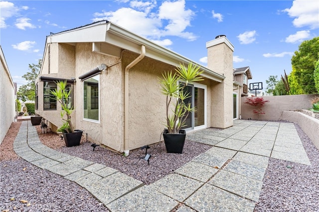view of property exterior featuring a patio area, stucco siding, a chimney, and fence