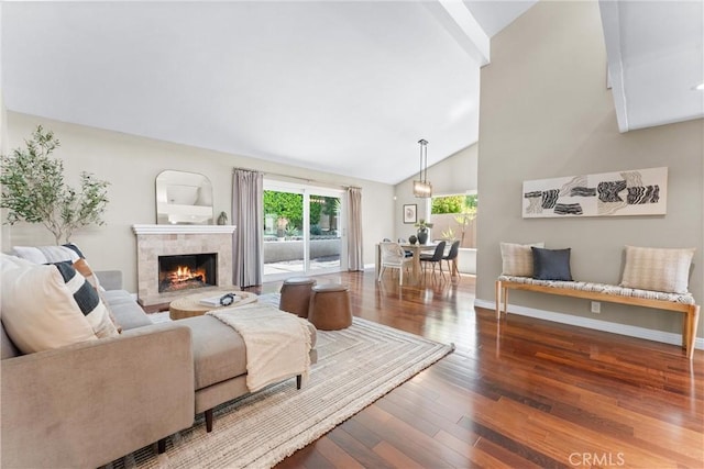 living room with beam ceiling, wood finished floors, a tile fireplace, baseboards, and high vaulted ceiling