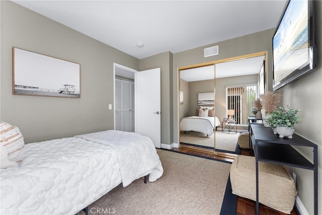 bedroom with a closet, baseboards, wood finished floors, and visible vents