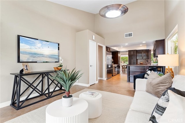 living room featuring baseboards, a wealth of natural light, a towering ceiling, and visible vents