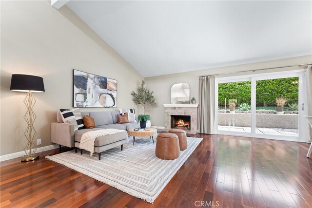 living area featuring baseboards, dark wood finished floors, a warm lit fireplace, and high vaulted ceiling