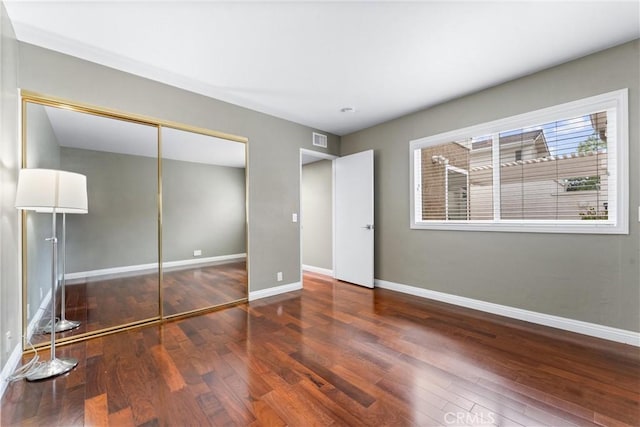 unfurnished bedroom with baseboards, wood finished floors, and a closet