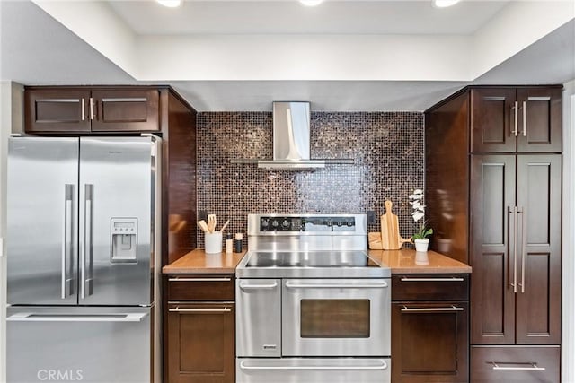 kitchen featuring wall chimney range hood, dark brown cabinets, light countertops, stainless steel appliances, and decorative backsplash