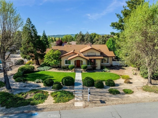 mediterranean / spanish house featuring a front yard, a chimney, a tile roof, and stucco siding