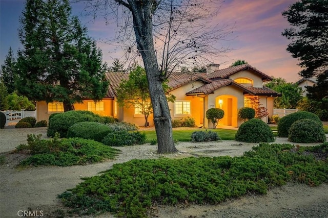 view of front facade featuring a tile roof, fence, and stucco siding