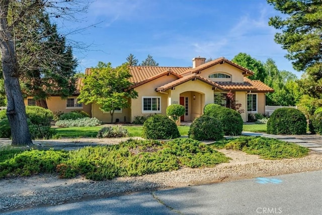 mediterranean / spanish house with stucco siding, a chimney, and a tile roof