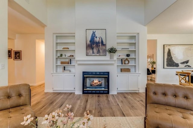 living area with built in features, wood finished floors, baseboards, and a glass covered fireplace