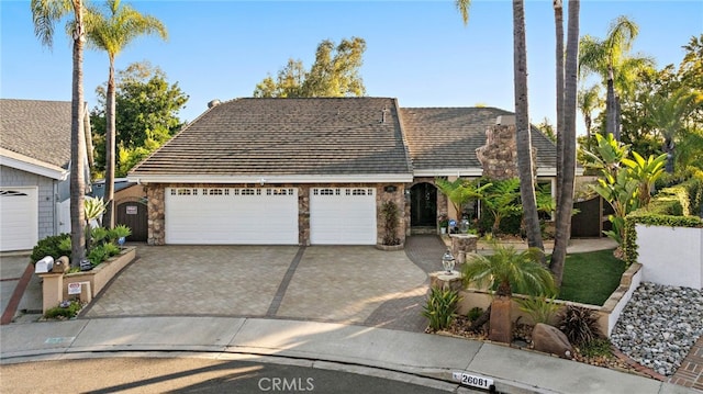view of front of property featuring stone siding, decorative driveway, and an attached garage