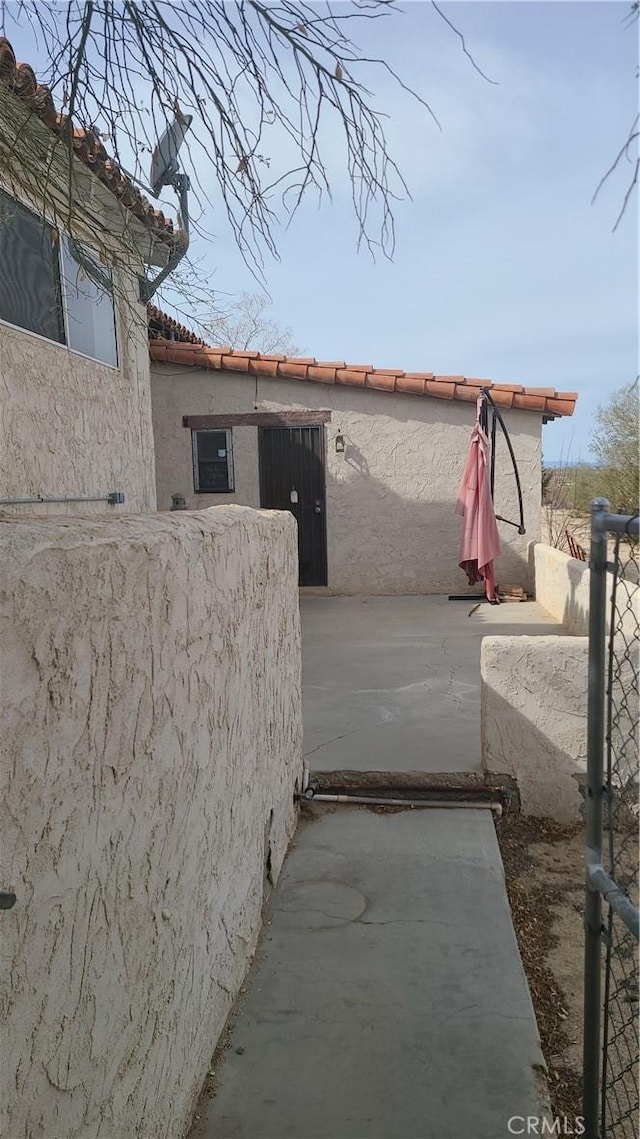 view of side of home with a tiled roof, fence, a patio, and stucco siding