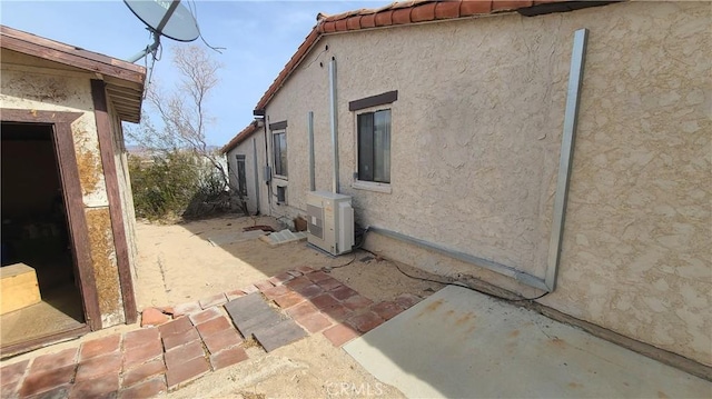 view of side of property with a tiled roof, ac unit, a patio, and stucco siding