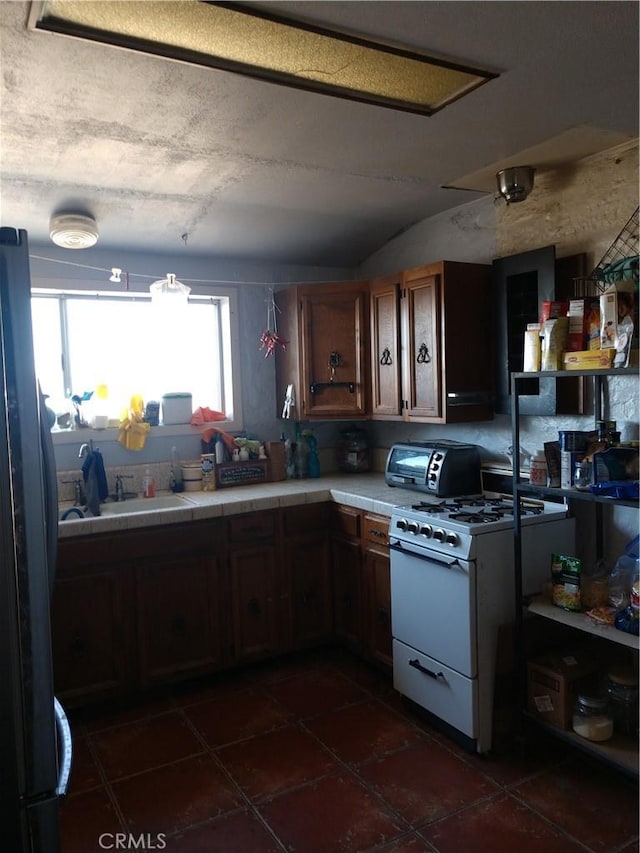 kitchen with dark tile patterned floors, white range with gas cooktop, a toaster, freestanding refrigerator, and tile countertops