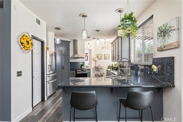 kitchen featuring a sink, wall chimney exhaust hood, dark stone counters, and stainless steel appliances