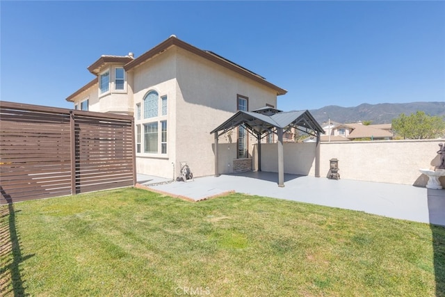 rear view of house with a mountain view, a patio area, a lawn, fence, and stucco siding