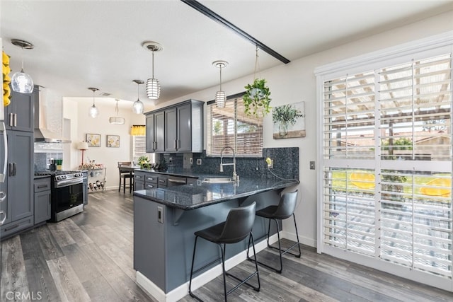 kitchen with tasteful backsplash, dark wood-style flooring, stainless steel range with gas cooktop, wall chimney exhaust hood, and a sink