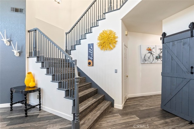 stairway with baseboards, a high ceiling, a barn door, visible vents, and wood finished floors