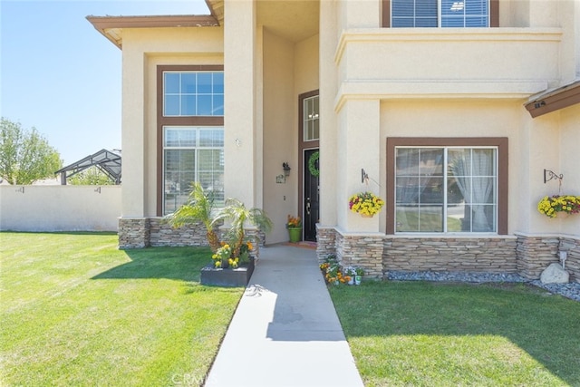 view of exterior entry featuring a yard, stone siding, and stucco siding