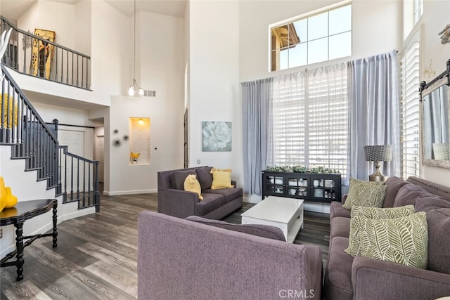 living area featuring a towering ceiling, baseboards, stairway, visible vents, and wood finished floors