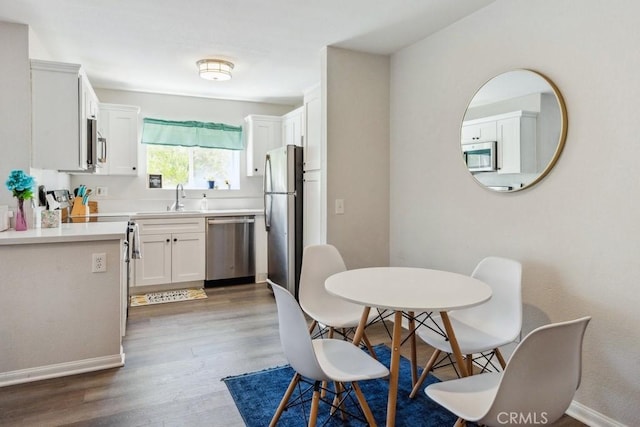 kitchen with white cabinets, a sink, stainless steel appliances, light countertops, and wood finished floors
