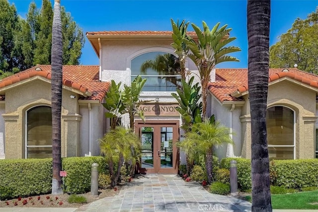 mediterranean / spanish-style home with stucco siding, a tiled roof, and french doors