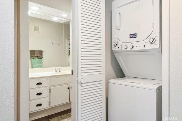 clothes washing area with visible vents, stacked washer and clothes dryer, laundry area, and a sink