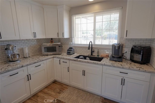kitchen with tasteful backsplash, light wood finished floors, a sink, and white cabinets