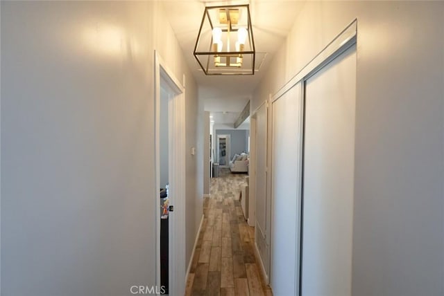 hall with baseboards, an inviting chandelier, and wood finished floors