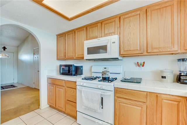 kitchen featuring arched walkways, tile countertops, light tile patterned floors, and white appliances