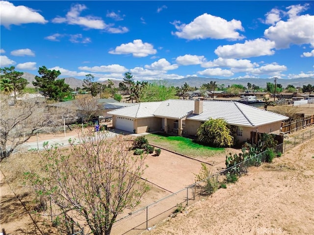rear view of house featuring a mountain view, stucco siding, fence, an attached garage, and driveway
