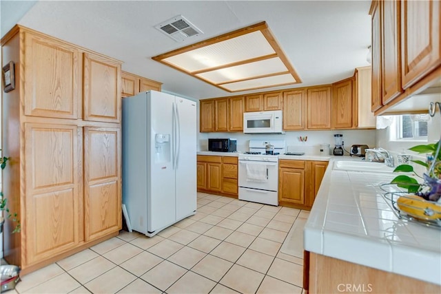 kitchen featuring visible vents, light tile patterned floors, a sink, white appliances, and tile countertops