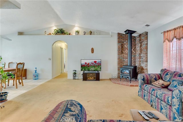 carpeted living area featuring arched walkways, visible vents, a wood stove, and vaulted ceiling