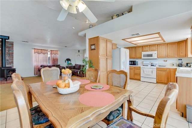 dining area with light tile patterned floors, visible vents, a wood stove, ceiling fan, and vaulted ceiling