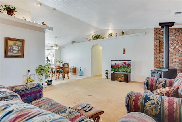 carpeted living area featuring a wood stove, ceiling fan, arched walkways, visible vents, and vaulted ceiling