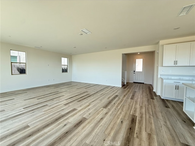 unfurnished living room with light wood-style flooring, baseboards, visible vents, and plenty of natural light