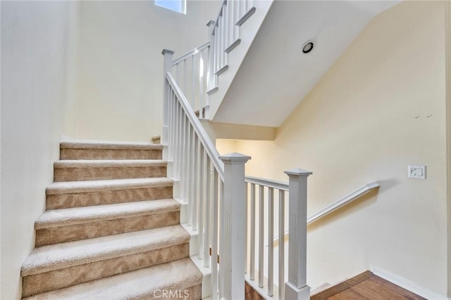 stairway featuring wood finished floors, a high ceiling, and baseboards