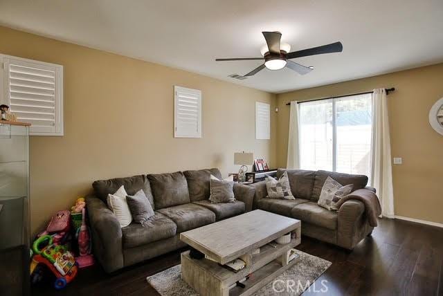 living room featuring baseboards, ceiling fan, and dark wood-type flooring