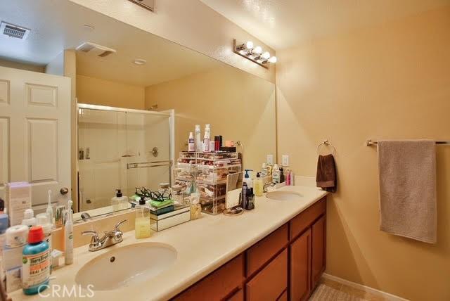 full bath with a sink, a shower stall, double vanity, and visible vents