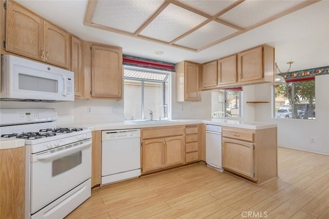 kitchen featuring light wood finished floors, light brown cabinets, white appliances, a peninsula, and light countertops